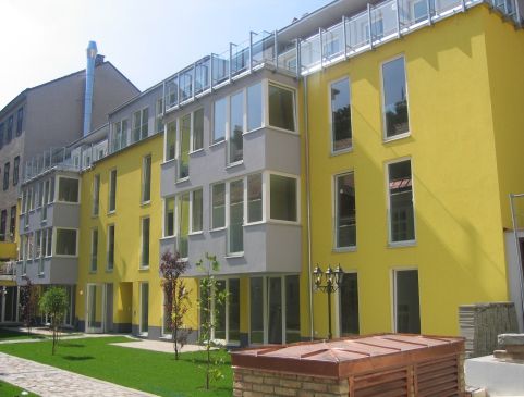 Neubau mit gelber Fassade und begrüntem Innenhof